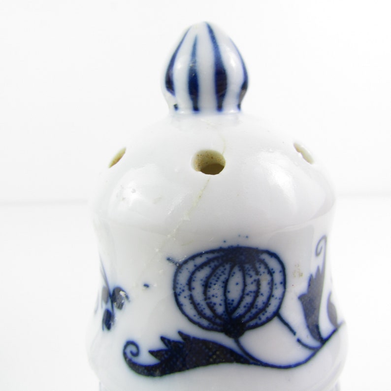 May include: White ceramic salt shaker with a blue and white floral design. The shaker has a small, round top with holes for dispensing salt.
