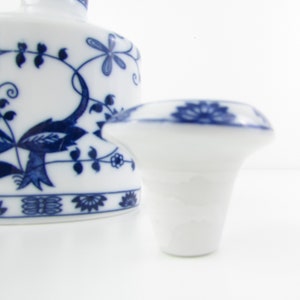 May include: A white porcelain bottle stopper with a blue floral design. The stopper has a round top and a flared base.