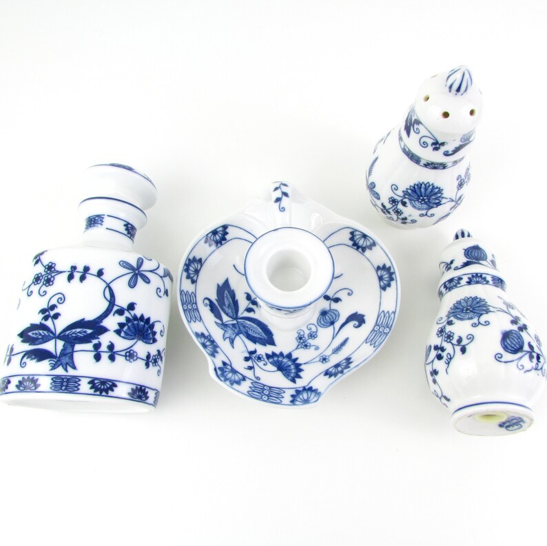 May include: A set of four blue and white porcelain pieces with a floral design. The set includes a candle holder, a salt shaker, a pepper shaker, and a small bottle.