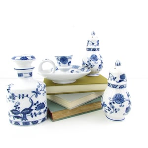 May include: A set of four blue and white porcelain pieces with floral designs. The set includes a candle holder, a salt shaker, a pepper shaker, and a bottle. The pieces are arranged on a stack of books.