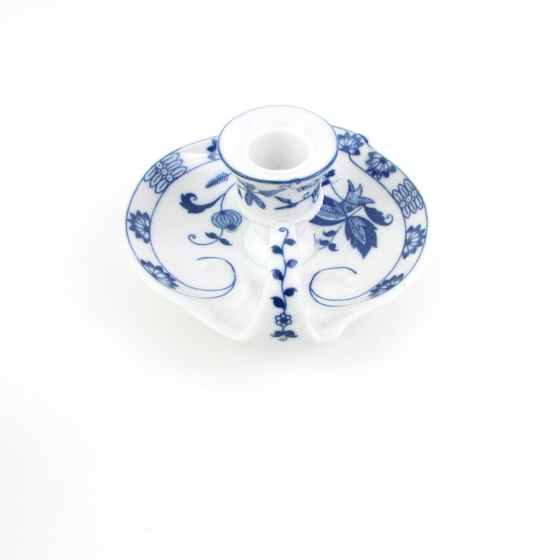 May include: White porcelain candle holder with a blue floral design. The holder has a round base and a single candle cup.