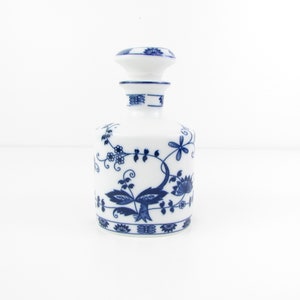 May include: A white porcelain bottle with a blue and white floral design. The bottle has a round body and a short neck with a lid.
