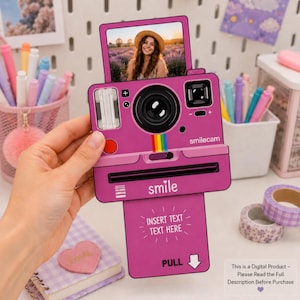 Op de afbeelding: Een magentakleurige kaart in de vorm van een instantcamera met een bovenframe met een foto van een persoon met een hoed, een centrale lens en een onderste uittrekbaar lipje met de tekst INSERT TEXT TEXT HERE en PULL.