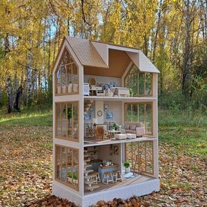 Peut inclure: Une maison de poupée à trois étages avec un toit brun clair et des murs beiges. La maison de poupée a de grandes fenêtres et est meublée avec des meubles miniatures. La maison de poupée est située à l'extérieur dans une zone boisée avec des feuilles d'automne.