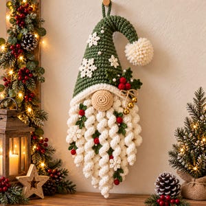 Può includere: Una decorazione da parete a forma di gnomo all'uncinetto con un alto cappello a punta verde decorato con fiocchi di neve bianchi e un pon-pon color crema. Lo gnomo ha un naso rotondo beige e una lunga barba bianca testurizzata con bacche rosse.