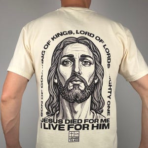 Könnte beinhalten: Cremefarbenes T-Shirt mit einer Schwarz-Weiß-Illustration von Jesus. Der Text um das Bild lautet: „SOHN GOTTES, KÖNIG DER KÖNIGE, HERR DER HERREN, MÄCHTIGER“. Unter dem Bild steht: „JESUS STARB FÜR MICH, ICH LEBE FÜR IHN“.