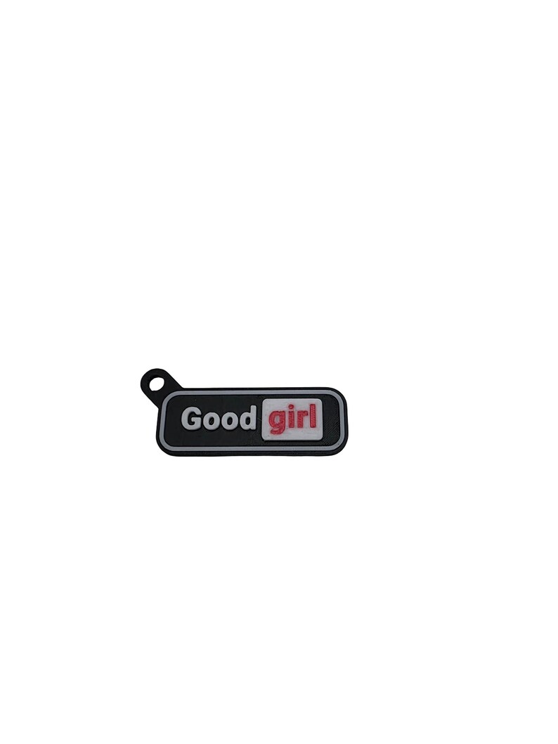 May include: A black rectangular charm with the words "Good girl" in white and red lettering. The charm has a small loop at the top for attachment.