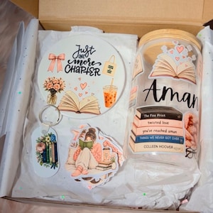 May include: A gift box containing a round ceramic coaster with the text Just one more chapter, a glass tumbler with a bamboo lid featuring book-themed decals and the name Aman, a rectangular keychain with a floral book stack, and a sticker.