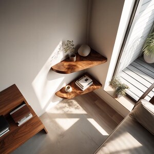 May include: Two wooden corner shelves with a natural wood grain are mounted on a white wall. The top shelf holds a decorative stone and a small plant. The bottom shelf displays books and a small ceramic cup. The shelves are in a room with a window and a wooden table.