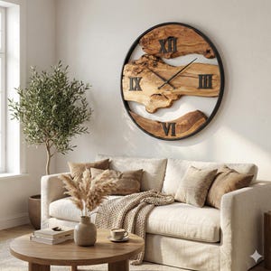 Puede incluir: Un gran reloj de pared redondo con una esfera de madera natural y números romanos negros. El reloj está enmarcado en un marco de metal negro. El reloj está montado en una pared blanca sobre un sofá color crema. Las manecillas del reloj son negras.