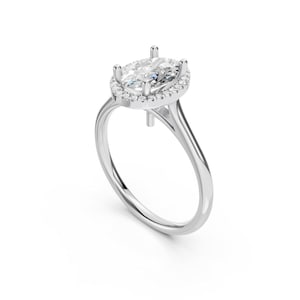 Puede incluir: Un anillo de plata con una piedra central de diamante de forma ovalada. El diamante está rodeado por un halo de diamantes más pequeños. El anillo tiene un diseño delicado de caña dividida.