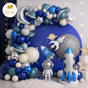 Peut inclure: Décoration de fête sur le thème de l'espace avec une arche de ballons bleus, blancs et argentés. Comprend une toile de fond avec des planètes et des fusées, une figurine d'astronaute argentée et une fusée spatiale.