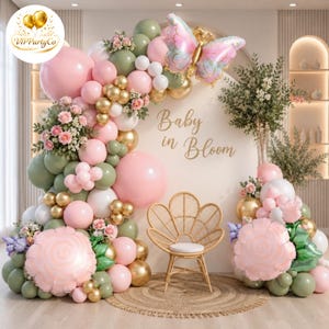 Puede incluir: Un arco de globos decorativo con globos rosas, dorados, blancos y verdes, flores y una mariposa. Las palabras "Baby in Bloom" están escritas en la pared. Una pequeña silla de mimbre está frente al arco.