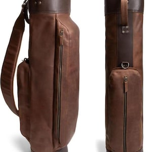 Puede incluir: Una bolsa de golf de cuero marrón con una correa para el hombro y un bolsillo lateral. La bolsa tiene una parte superior e inferior de color marrón oscuro, con una cremallera en el lateral. La bolsa está diseñada para guardar palos y accesorios de golf.