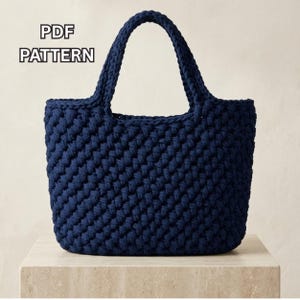 Puede incluir: Un bolso de ganchillo azul marino oscuro con un patrón de puntadas gruesas y texturizadas y dos asas integradas. El texto "PDF PATTERN" es claramente visible en la esquina superior izquierda, indicando que es un documento de diseño digital.
