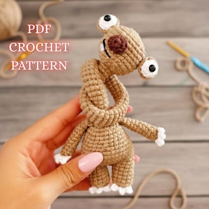 May include: A crocheted brown alien-like creature with large, googly eyes and white accents. The text "PDF CROCHET PATTERN" is visible in the upper left corner. The handmade toy is held in a hand.