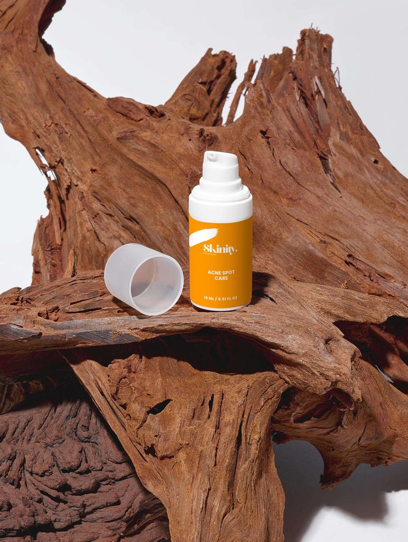 May include: A skincare product bottle with a white pump and a bright yellow label. The label reads "Skinity. Acne Spot Care" and the bottle is 15 ml / 0.51 fl oz. The bottle is next to its cap, and both are on a textured, brown wooden surface.