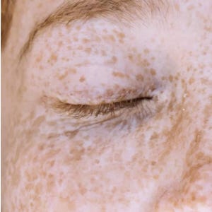 May include: Close-up of a person's closed eye and eyebrow. The skin is light-toned with numerous freckles. The eyebrow is a light brown color, and the eyelashes are visible. The overall image has a soft, natural aesthetic.