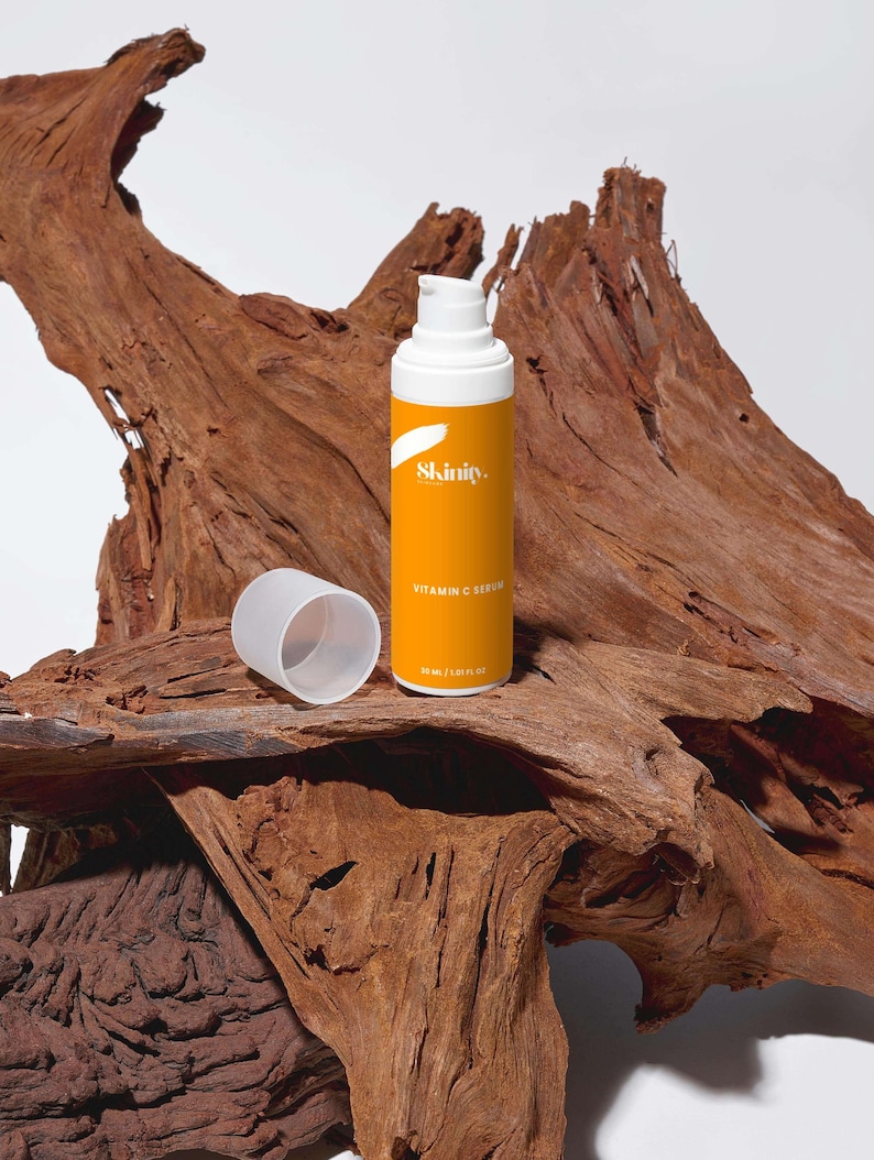 K&ouml;nnte beinhalten: Eine orange-wei&szlig;e Vitamin-C-Serumflasche mit dem Markennamen "Skinity" und dem Text "Vitamin C Serum" auf dem Etikett. Die Flasche enth&auml;lt 30 ml. Der Deckel ist abgenommen und liegt neben der Flasche. Der Hintergrund ist ein St&uuml;ck strukturiertes Holz.