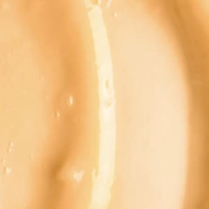 May include: Close-up of a smooth, light orange-yellow liquid with a glossy sheen. The surface has gentle, flowing curves and subtle variations in tone, creating a sense of depth and texture. The overall effect is one of fluidity and richness.