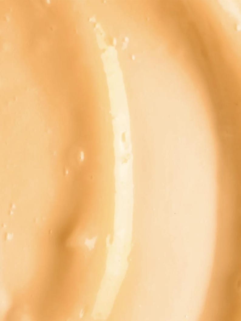 May include: Close-up of a smooth, light orange-yellow liquid with a glossy sheen. The surface has gentle, flowing curves and subtle variations in tone, creating a sense of depth and texture. The overall effect is one of fluidity and richness.