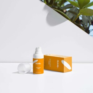 May include: An orange skincare product bottle and box with the brand name "Skinity" and the words "Acne Spot Care". The bottle is white with a pump dispenser. The box is rectangular and has a white brushstroke design.