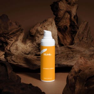 K&ouml;nnte beinhalten: Eine wei&szlig;e und orangefarbene Vitamin-C-Serumflasche mit dem Markennamen "Skinity" und Produktdetails. Die Flasche steht vor einem Hintergrund aus dunkelbraunen Holzst&uuml;cken. Die Serumflasche enth&auml;lt 30 ml / 1,01 fl oz.