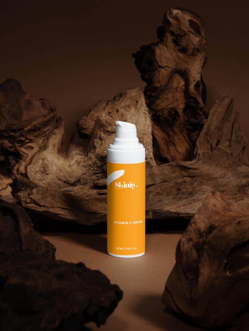K&ouml;nnte beinhalten: Eine wei&szlig;e und orangefarbene Vitamin-C-Serumflasche mit dem Markennamen "Skinity" und Produktdetails. Die Flasche steht vor einem Hintergrund aus dunkelbraunen Holzst&uuml;cken. Die Serumflasche enth&auml;lt 30 ml / 1,01 fl oz.
