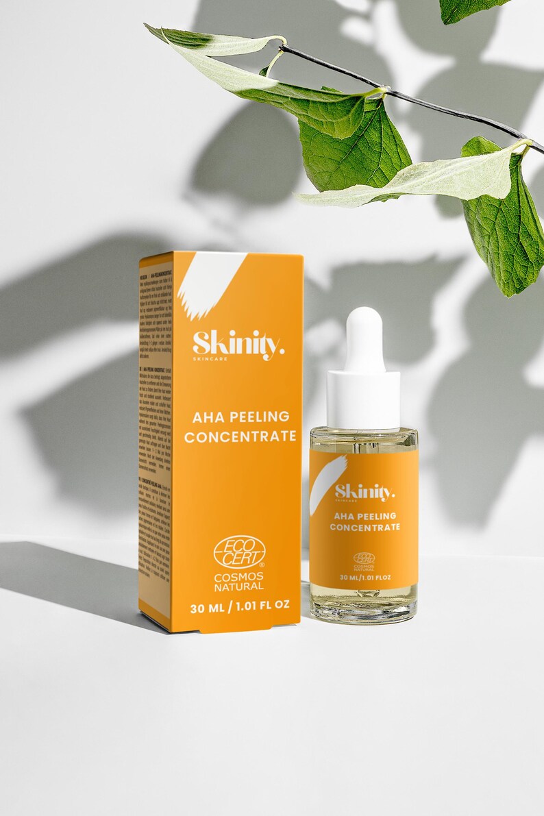K&ouml;nnte beinhalten: Eine orangefarbene Schachtel und eine transparente Glasflasche mit Hautpflegeprodukten werden vor einem wei&szlig;en Hintergrund mit gr&uuml;nen Bl&auml;ttern gezeigt. Auf der Schachtel und der Flasche steht der Markenname "Skinity" und der Text "AHA Peeling Concentrate". Die Flasche enth&auml;lt 20 ml.