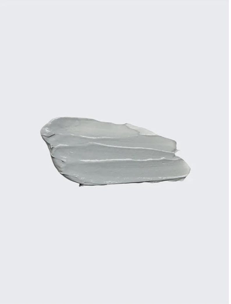 May include: A smear of light gray cosmetic product, possibly a mask or cream, against a white background. The product is thick and has visible texture from application, with several horizontal strokes. The overall appearance is smooth and opaque.