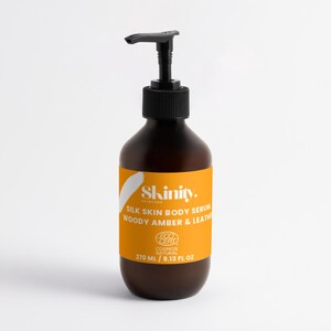 May include: A brown bottle of Skinity Silk Skin Body Serum with a black pump dispenser. The label is orange with white text and a white brushstroke design. The bottle contains 9.13 fl oz (270 ml) of serum.