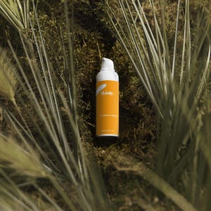 K&ouml;nnte beinhalten: Eine Hautpflegeproduktflasche mit wei&szlig;em Pumpkopf und orangefarbenem Etikett. Auf dem Etikett steht "Skinity" und "Vitamin C Serum". Die Flasche befindet sich vor einem Hintergrund aus gr&uuml;nem Laub.