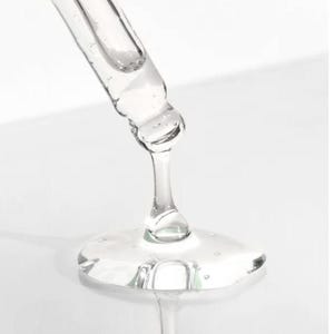 K&ouml;nnte beinhalten: Nahaufnahme einer transparenten Glaspipette, die eine z&auml;hfl&uuml;ssige, transparente Fl&uuml;ssigkeit abgibt. Die Fl&uuml;ssigkeit bildet eine kleine, flache Pf&uuml;tze mit reflektierender Oberfl&auml;che. Der Hintergrund ist hell und wei&szlig;, was die Klarheit des Produkts hervorhebt.