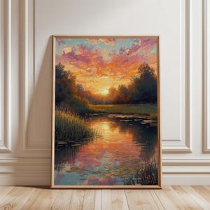 May include: A framed landscape painting depicts a sunset over a calm lake. The sky is filled with vibrant orange, pink, and blue hues, reflecting in the water. Trees line the banks, and tall grass grows along the water's edge.