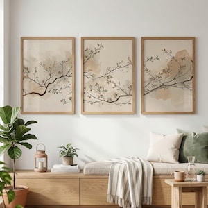 Puede incluir: Tres impresiones artísticas enmarcadas con ramas de estilo acuarela con hojas en tonos marrón y beige. La obra de arte está sobre un fondo neutro, y los marcos son de madera clara. Las impresiones se exhiben sobre un banco de madera.