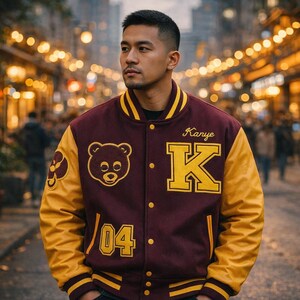 May include: A maroon and gold varsity jacket with the name "Kanye" and the letter "K" in gold lettering. The jacket features a bear patch and the number "04". The sleeves are gold.