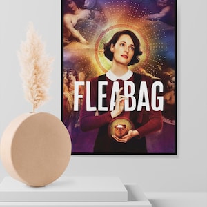 May include: A framed poster featuring the word "FLEABAG" in large white letters. The image depicts a woman in a burgundy dress with a white collar, holding a small, round object. The background includes religious-style artwork.