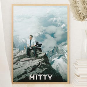 以下が含まれることがあります： 山頂に座り、ブリーフケースと飲み物を持っている男性が描かれた額入りのポスター。ポスターには「THE SECRET LIFE OF WALTER MITTY」というテキストと「MITTY」という名前が記載されています。背景には山脈が描かれています。