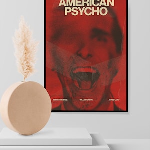 Könnte beinhalten: Ein gerahmtes Poster mit dem Titel "AMERICAN PSYCHO" in fetten, weißen Buchstaben auf rotem Hintergrund. Das Poster zeigt ein verzerrtes Bild eines Gesichts mit offenem Mund. Die Namen Christian Bale, Willem Dafoe und Jared Leto sind unten aufgeführt.