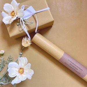 May include: A brown gift box tied with a white ribbon and a tag, alongside a roll of brown paper. The image is decorated with white and yellow flowers. The paper roll has text that reads: Eco Friendly Recycled Quality, Pure Kraft Paper, 100% Recyclable & Biodegradable.