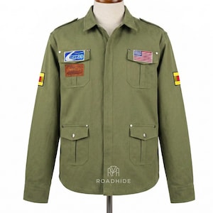 Könnte beinhalten: Olivgrüne Jacke mit mehreren Taschen und Aufnähern. Mit einem US-Flaggen-Aufnäher und einem Aufnäher mit dem Text "EAST END". Die Jacke hat eine Knopfleiste vorne und einen Kragen. Die Jacke hat gelbe und rote Aufnäher auf den Ärmeln.