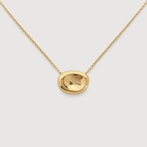 May include: A gold-toned necklace featuring a delicate chain and a single, smooth, polished, pebble-shaped pendant. The pendant has a rounded, organic form with a reflective surface that catches the light, suspended centrally from the thin chain.