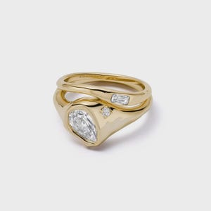 Peut inclure: Une bague en or au design fluide et organique, ornée d'une grande pierre claire en forme de poire, d'une pierre claire rectangulaire de taille baguette et d'une minuscule pierre claire ronde sertie dans le métal en or jaune poli.
