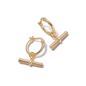 May include: A pair of gold-toned hoop earrings featuring a dangling horizontal bar charm. Each bar has a textured, diagonal ribbed surface. The hoops are circular with a hinged closure mechanism, and the entire set is finished in a polished gold tone.