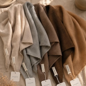 May include: A collection of five soft wool scarves in shades of cream, light grey, medium brown, dark brown, and tan. Each scarf features a white fabric tag labelled 100% WOOL and a square white paper hang tag with the brand name ELVA ROSE printed.