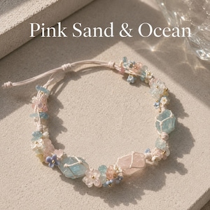 May include: A bracelet featuring pink and light blue stones, small flower-shaped beads, and gold accents on a light pink cord. The text Pink Sand & Ocean is visible above the bracelet, which has an adjustable sliding knot closure.