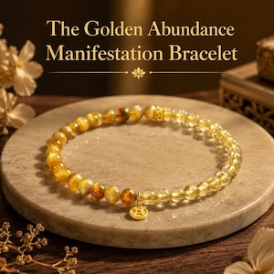 Puede incluir: Una pulsera dorada con cuentas doradas y un pequeño dije dorado. La pulsera está hecha de cuentas redondas de color amarillo dorado y se exhibe sobre una superficie de piedra redonda y clara. El texto "The Golden Abundance Manifestation Bracelet" está en la parte superior.