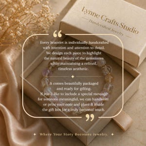 May include: A handcrafted gemstone bracelet inside a gift box. The box is beige with the text "Lynne Crafts Studio Handcrafted Jewelry." The bracelet features various colored stones. The box is on a satin surface.
