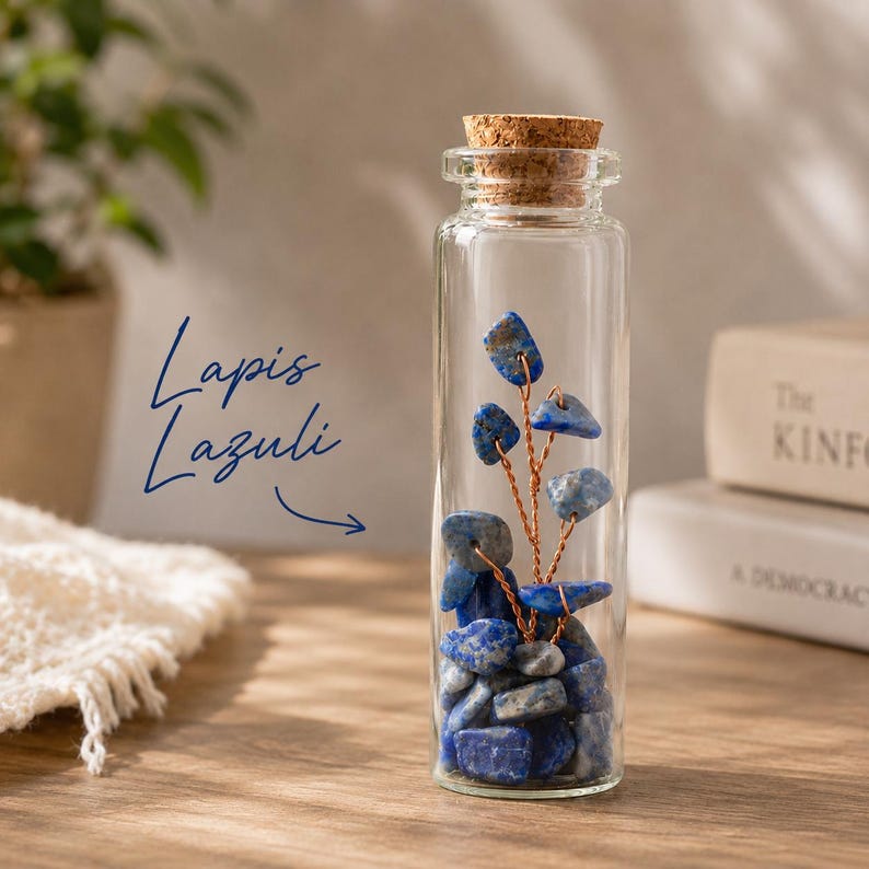 May include: A clear glass bottle filled with blue lapis lazuli stones and a copper wire tree. The bottle is topped with a cork stopper. The words "Lapis Lazuli" are written in blue script.