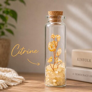 May include: A clear glass bottle with a cork stopper filled with yellow citrine crystals. A wire structure with citrine crystal accents is inside the bottle. The word "Citrine" is written in cursive on the left side of the image.